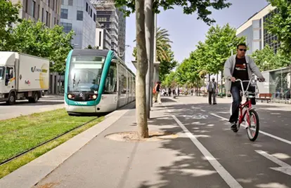 Image of a road with a truck, a person on a bicycle, a lightrail train