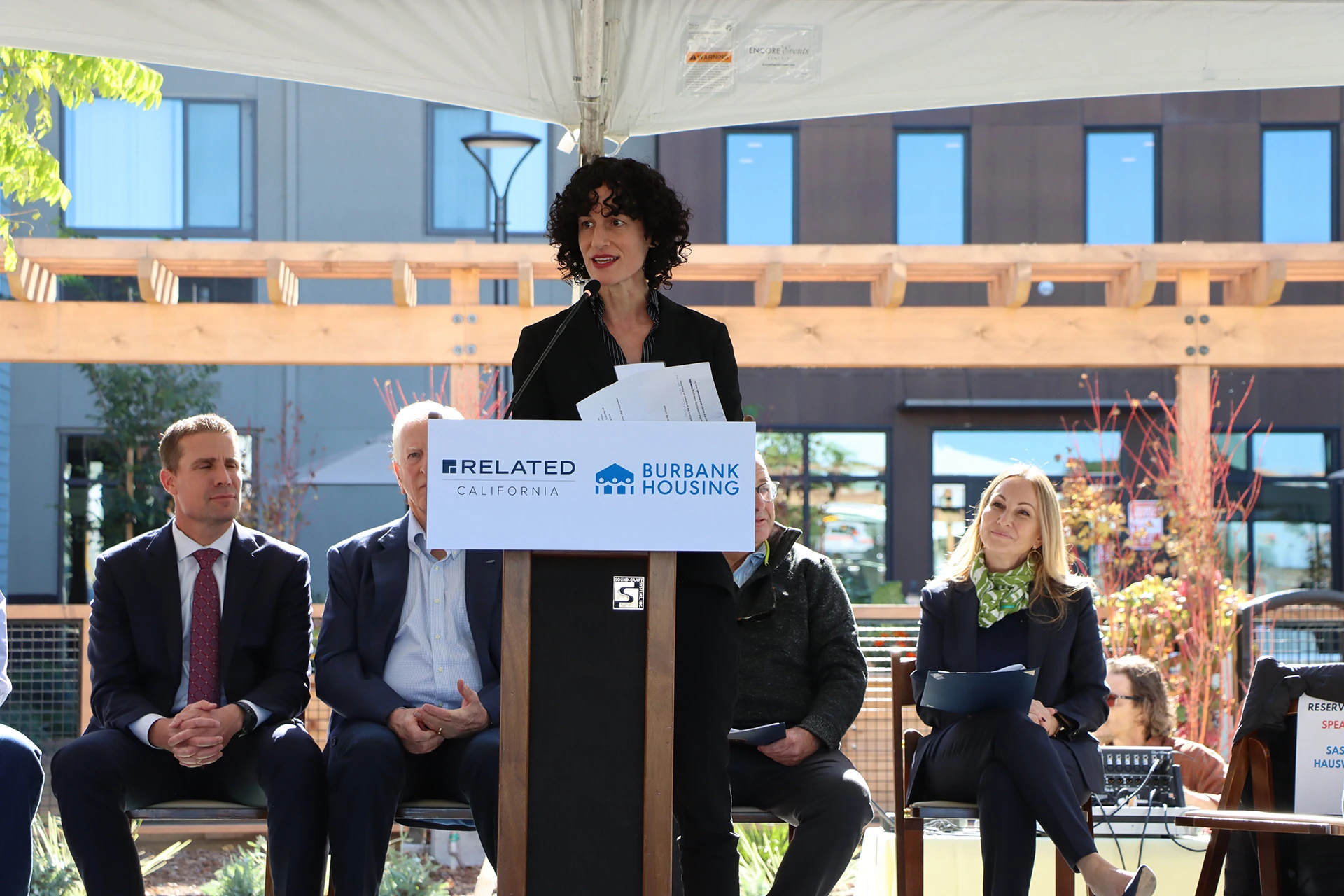 Photo of HCD Deputy Director Sasha Hauswald standing at a podium and speaking in front of Laurel at Perennial Park housing complex.